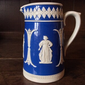 Può includere: Un'anfora in ceramica blu e bianca con manico bianco e disegni in rilievo bianchi di figure e motivi floreali.