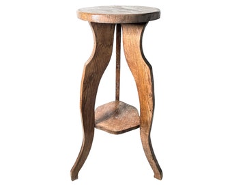 May include: A wooden plant stand with a round top and a lower shelf. The stand has three legs that curve outwards at the bottom.