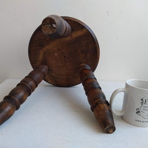 May include: A wooden stool with three turned legs and a round top. The stool is brown and has a rustic appearance.
