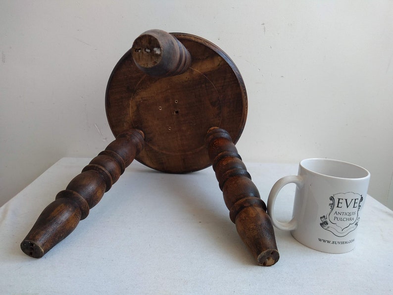 May include: A wooden stool with three turned legs and a round top. The stool is brown and has a rustic appearance.