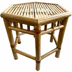 Könnte beinhalten: Ein sechseckiger Bambus-Beistelltisch mit einer Lattenoberfläche und filigranen Gitterarbeiten an den Seiten. Der Tisch hat eine natürliche Holzoptik und steht auf sechs Beinen.