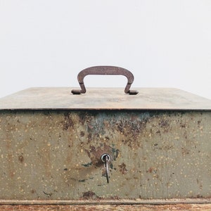May include: A vintage metal box with a rusty green finish and a metal handle. The box has a keyhole and a key in it.