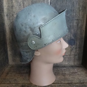 Könnte beinhalten: Ein grüner Metallhelm mit Visier und Riemen. Der Helm befindet sich auf einem Mannequin-Kopf.