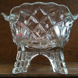 以下が含まれることがあります： ダイヤモンド模様と3本の脚が付いた透明なガラスのボウル。ボウルは木製の表面の上に置かれています。