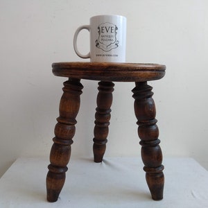 May include: A dark brown wooden stool with three turned legs. The stool has a round top and is about 18 inches tall.