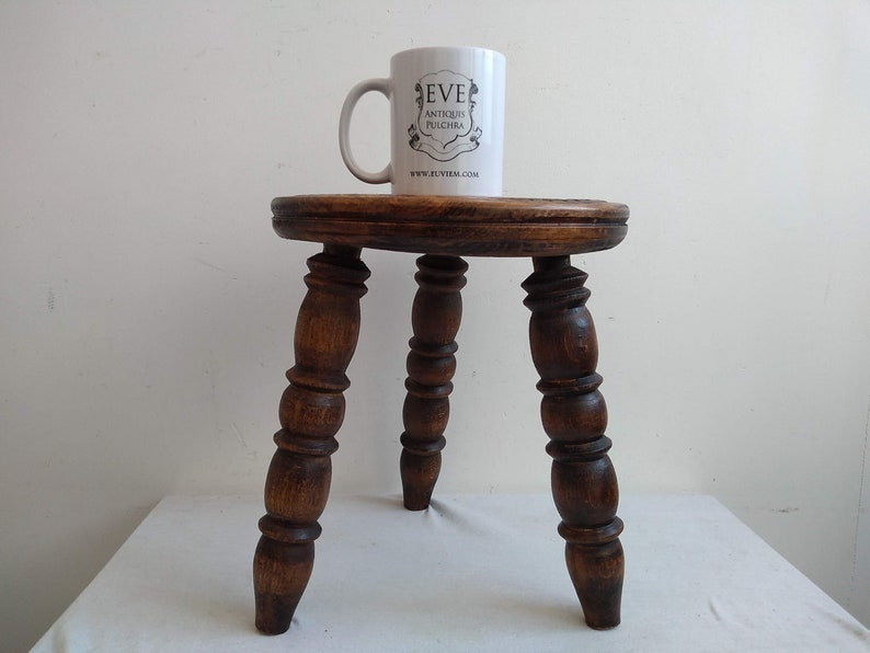 May include: A dark brown wooden stool with three turned legs. The stool has a round top and is about 18 inches tall.