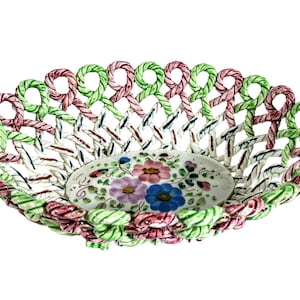 May include: A white ceramic bowl with a woven design in pink, green, and blue. The bowl has a floral pattern in the center.