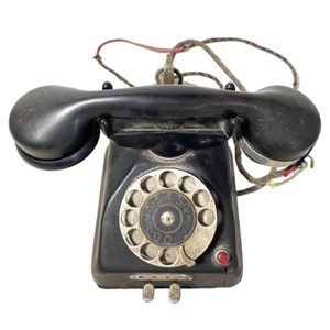 May include: A black rotary dial phone with a black handset and a white dial. The phone has a cord attached to it.
