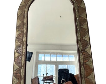 May include: An arched mirror with a decorative frame made of copper and silver. The frame features a repeating pattern of overlapping crescent shapes.