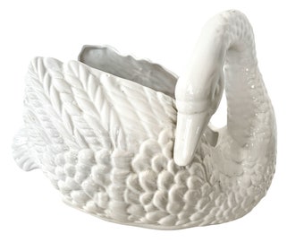 May include: White ceramic swan planter with a detailed feathered design. The swan's neck is curved and the head is tilted down. The planter is designed to hold plants or flowers.