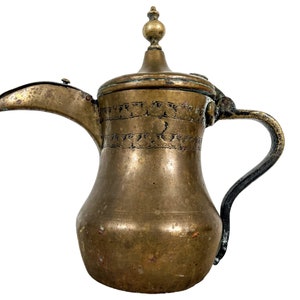 May include: A brass teapot with a hinged lid and a decorative handle. The teapot has an ornate design etched into the surface.