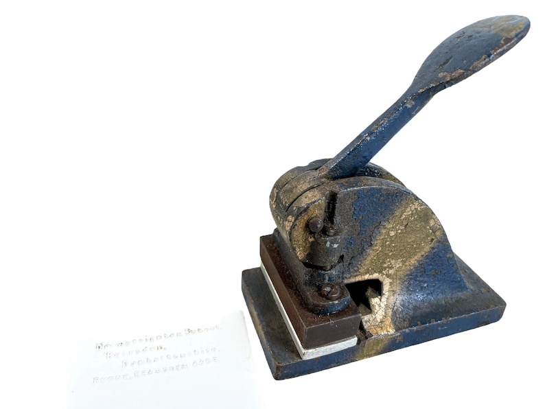 May include: A vintage blue and gold metal letter press with a lever handle. The letter press is sitting on a white surface with a piece of paper underneath it. The paper has text on it that reads "Dear President Truman, I received your letter..."