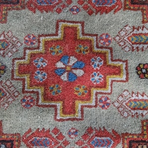 May include: A close-up of a colorful rug with a geometric pattern. The rug is made of wool and has a soft, textured surface. The colors in the rug are red, blue, yellow, and white.