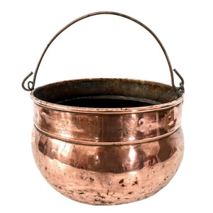 Pode incluir: Uma panela de cobre vintage com uma alça de arame. A panela tem um fundo arredondado e uma abertura larga. Tem um aspecto desgastado e envelhecido.