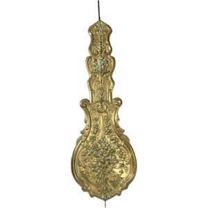Könnte beinhalten: Ein verziertes, goldfarbenes Dekorpendel für eine Uhr. Das Pendel ist tropfenförmig mit aufwendigen floralen Mustern.