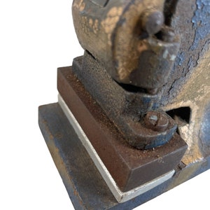 May include: Close-up of a vintage metal hand press with a blue and brown paint finish. The press has a lever and a base with a rectangular opening.