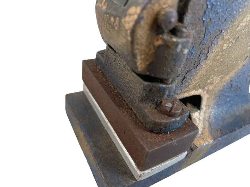 May include: Close-up of a vintage metal hand press with a blue and brown paint finish. The press has a lever and a base with a rectangular opening.