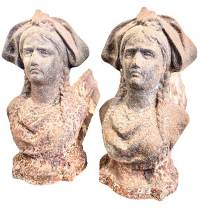Puede incluir: Dos esculturas de terracota desgastadas de bustos de mujeres con tocados elaborados. Las esculturas están en un estilo desgastado y rústico, con una paleta de colores marrón y gris.