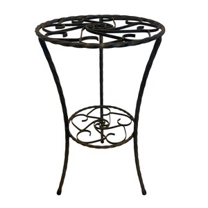May include: A dark brown wrought iron plant stand with a circular top and a lower circular shelf. The top and shelf feature decorative scrollwork. The stand has three curved legs and a central support.