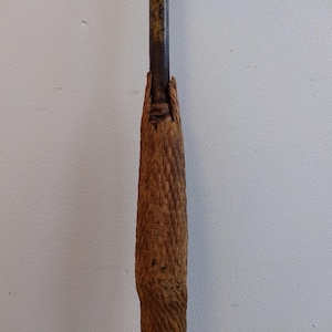 May include: A close-up of the handle of a wooden spear. The handle is wrapped in a woven material and is secured with a metal band.