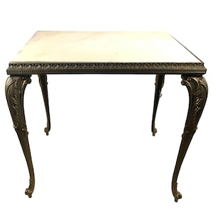 Puede incluir: Una mesa dorada con patas ornamentadas y una tapa de mármol blanco. La mesa tiene un borde decorativo alrededor del borde de la tapa.