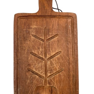 Può includere: Un tagliere in legno vintage con un design ad albero intagliato e una piccola forma di mela intagliata. Il tagliere ha un aspetto usurato e rustico ed è fatto di legno marrone scuro.