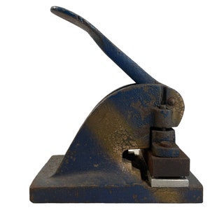 May include: A blue and gold metal hand-operated stamp with a lever. The stamp has a rectangular base and a lever that is attached to a metal plate.