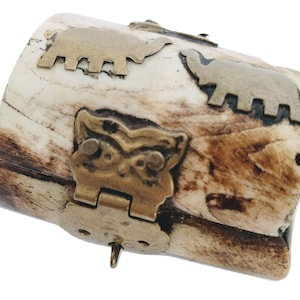 Puede incluir: Una pequeña caja cilíndrica hecha de hueso con un cierre de latón y diseños decorativos de elefantes y búhos de latón.