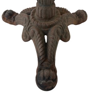 May include: A close-up of the base of a cast iron table with three legs. The legs are intricately designed with a rope-like pattern and a decorative ball at the end of each leg.