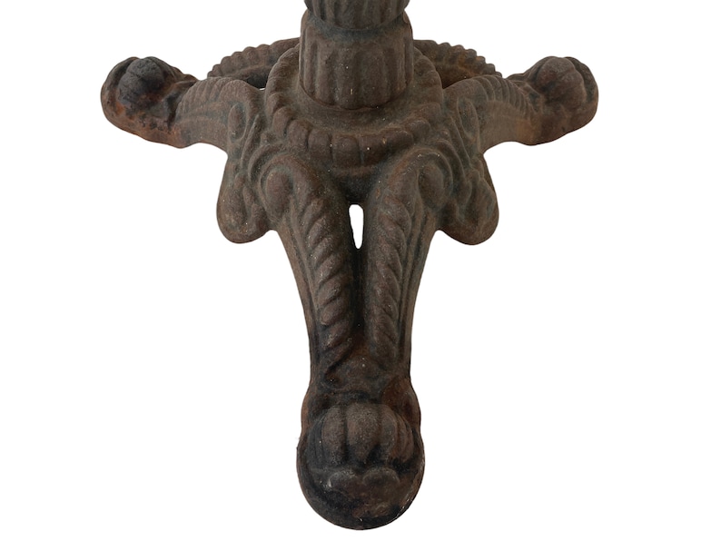 May include: A close-up of the base of a cast iron table with three legs. The legs are intricately designed with a rope-like pattern and a decorative ball at the end of each leg.