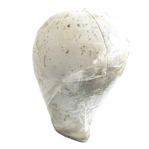 May include: A white fabric mannequin head covered in clear plastic wrap. The fabric is slightly dirty and has brown spots.