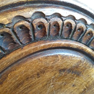 May include: Close-up of a wooden plate with a carved, decorative edge. The edge features a repeating pattern of small, rounded shapes with a hole in the center.