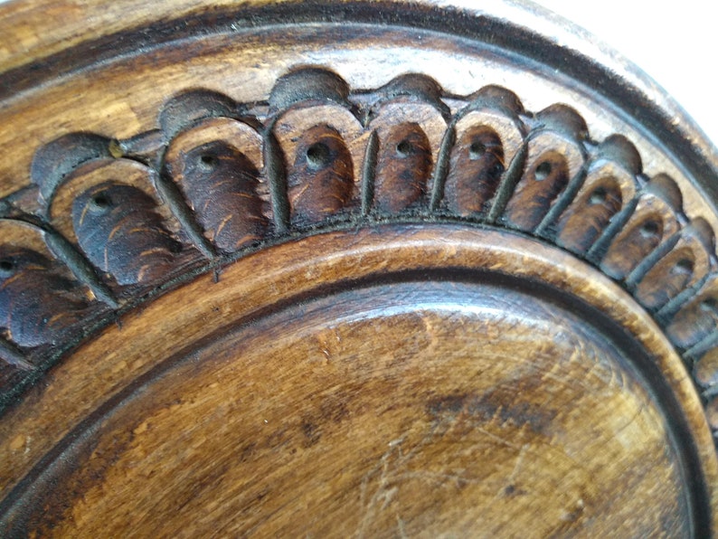 May include: Close-up of a wooden plate with a carved, decorative edge. The edge features a repeating pattern of small, rounded shapes with a hole in the center.