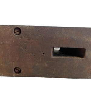 May include: A dark brown wooden block with a rectangular cutout and two visible screws. The block has a worn, rustic appearance.