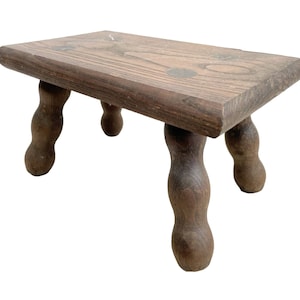 May include: A small wooden stool with four turned legs. The stool is made of dark brown wood and has a rectangular top.