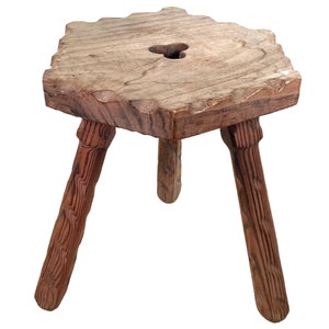 May include: A rustic wooden stool with three legs and a heart-shaped cutout in the top. The stool is made of rough-hewn wood and has a natural brown finish.