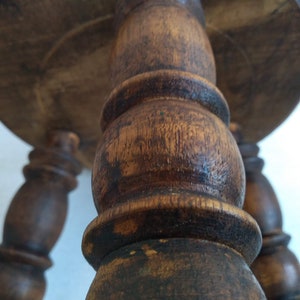 May include: A wooden stool with three turned legs and a round top. The legs are dark brown and have a worn finish.
