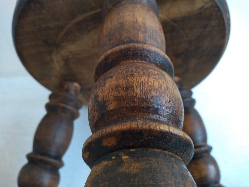 May include: A wooden stool with three turned legs and a round top. The legs are dark brown and have a worn finish.