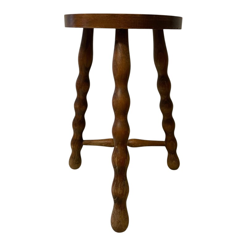 K&ouml;nnte beinhalten: Ein kleiner, dreibeiniger Holzschemel mit rundem Sitz. Die Beine sind aufwendig mit einem gedrehten, seilartigen Design geschnitzt. Der Hocker ist aus warmem, mittelget&ouml;ntem Holz gefertigt und zeigt die nat&uuml;rliche Maserung.