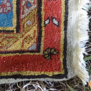 May include: Close-up of the edge of a rug with a red, gold, and blue pattern. The rug has a fringe border and is made of a soft, woven material.