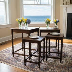 May include: A set of four dark brown wooden nesting tables with turned legs. Each table has a square top, and they vary in size. The tables are arranged on a patterned rug, with vases of flowers and plates on top.