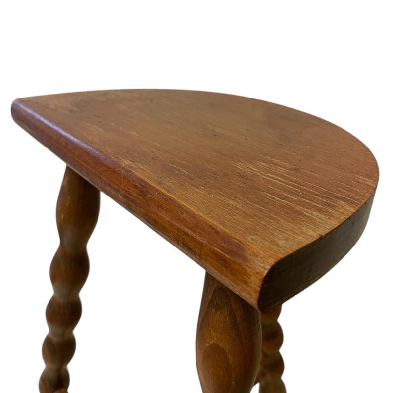 K&ouml;nnte beinhalten: Kleiner Beistelltisch aus Holz mit halbmondf&ouml;rmiger Platte. Der Tisch hat drei Beine, von denen zwei aufwendig mit einem Spiralmuster geschnitzt sind. Das Holz hat einen warmen, braunen Farbton und eine sichtbare Maserung.