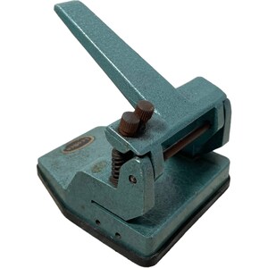 Könnte beinhalten: Ein vintage blauer Papierlocher aus Metall mit einem Hebelgriff und einem Metallfuß. Der Locher hat ein Etikett mit der Aufschrift "La Corona".