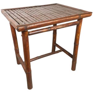 May include: A small, square bamboo table with a slatted top and four angled legs. The table is made of dark brown bamboo and has a natural, rustic appearance. The table is approximately 24 inches long, 24 inches wide, and 20 inches tall.