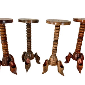 Könnte beinhalten: Vier Holzhocker mit einem einzigartigen Design. Jeder Hocker hat eine runde Oberseite und eine Basis, die einem Paar Holzschuhe ähnelt. Die Hocker sind aus dunkelbraunem Holz gefertigt und haben eine natürliche Oberfläche.