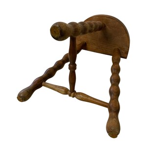K&ouml;nnte beinhalten: Ein kleiner, antiker Holzschemel. Der Schemel hat eine runde Sitzfl&auml;che und gedrechselte Beine, die alle aus hellbraunem Holz gefertigt sind. Die Beine haben ein dekoratives, geschnitztes Design. Dieser Vintage-Hocker w&auml;re eine charmante Erg&auml;nzung f&uuml;r jeden Raum.