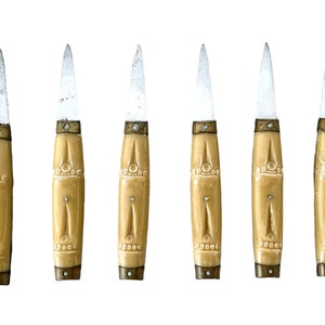 May include: Set of six small, ornate knives with ivory-colored handles and silver blades. The handles have intricate carvings and gold accents.