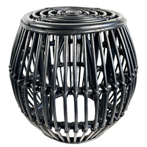 May include: Black woven rattan stool with a round top and a spherical base. The stool is made of natural materials and has a rustic, bohemian style.