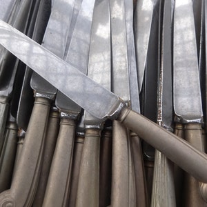 Peut inclure: Gros plan sur un groupe de couteaux en argent avec des manches. Les couteaux sont disposés en éventail, les lames pointant vers le centre de l'image. Les manches sont tous faits du même matériau et ont une forme légèrement incurvée.