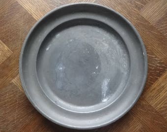 Puede incluir: Un plato redondo de metal gris con un borde elevado. El plato tiene una superficie lisa ligeramente texturizada.